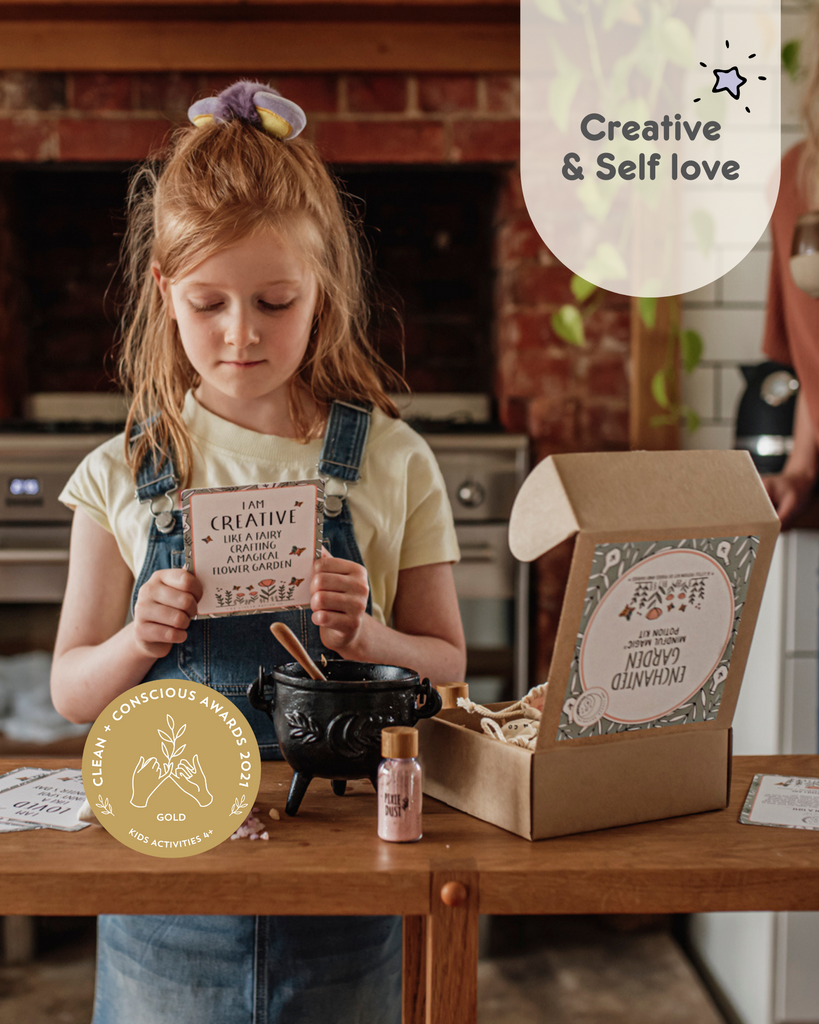 Enchanted Garden fairy potion kit. Image shows a girl standing in kitchen reading a potion affriamtion cards that reads I am Creative like a fairy crafting a magical flower garden. There is also a cauldron , a potion bottle of pixie dust and the enchanted garden potion kit box opened. 
