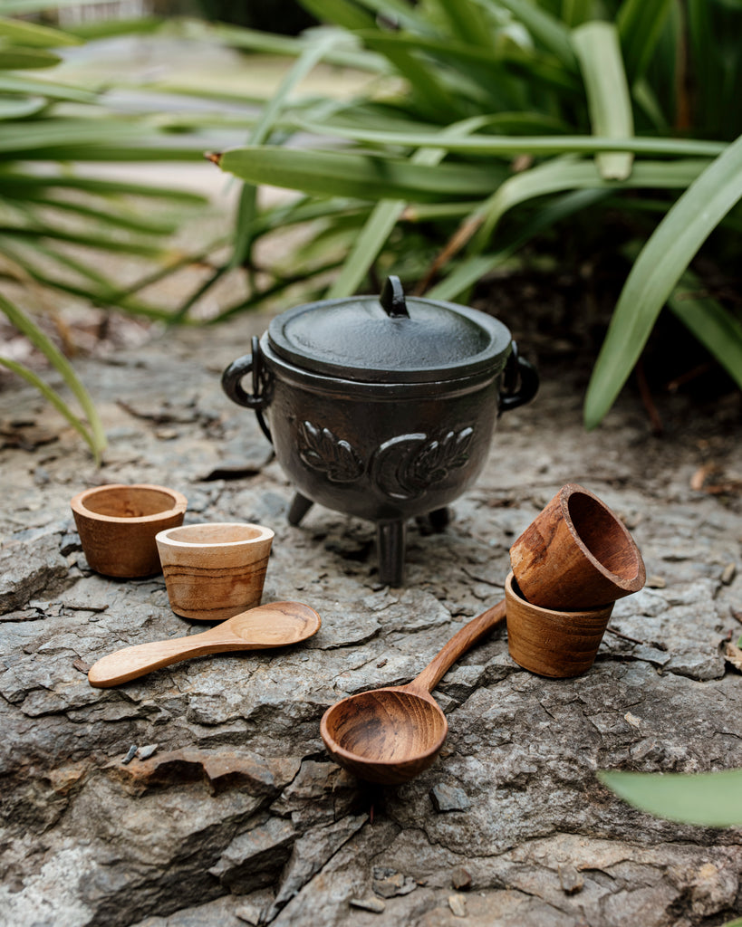 Black cauldron with wooden spoon inside, wooden pots and mini spoon