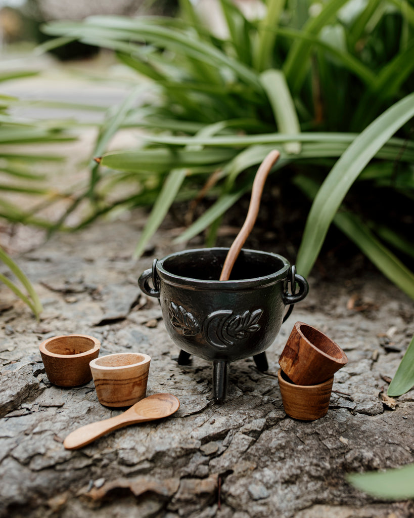 Black cauldron with wooden spoon inside, wooden pots and mini spoon