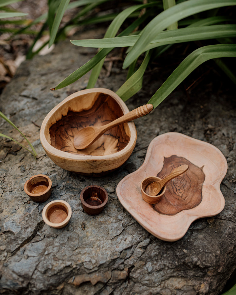 wooden bowl, plate, 4 wooden mini bowls and a spoon on a slate rock